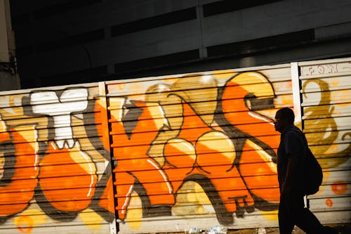Free Unrecognizable man strolling near wall with graffiti Stock Photo
