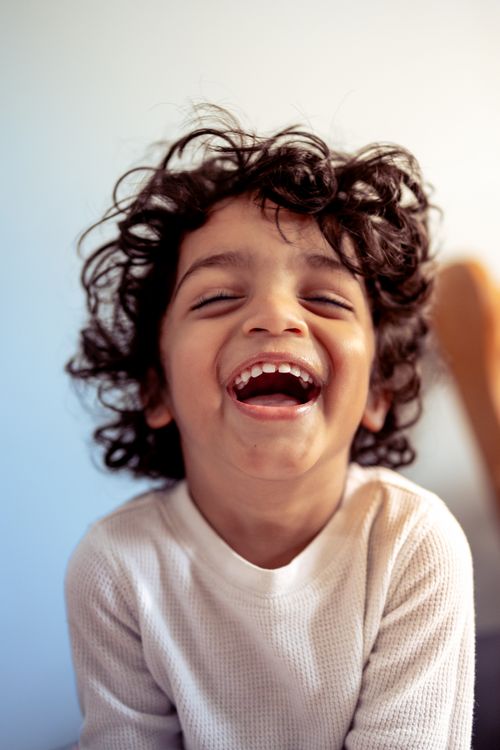 Free A young child with curly hair smiling broadly, exuding happiness in an indoor setting. Stock Photo