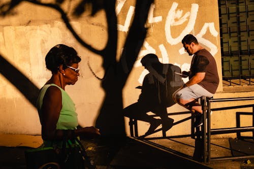 Ethnic man using smartphone while senior woman walking by