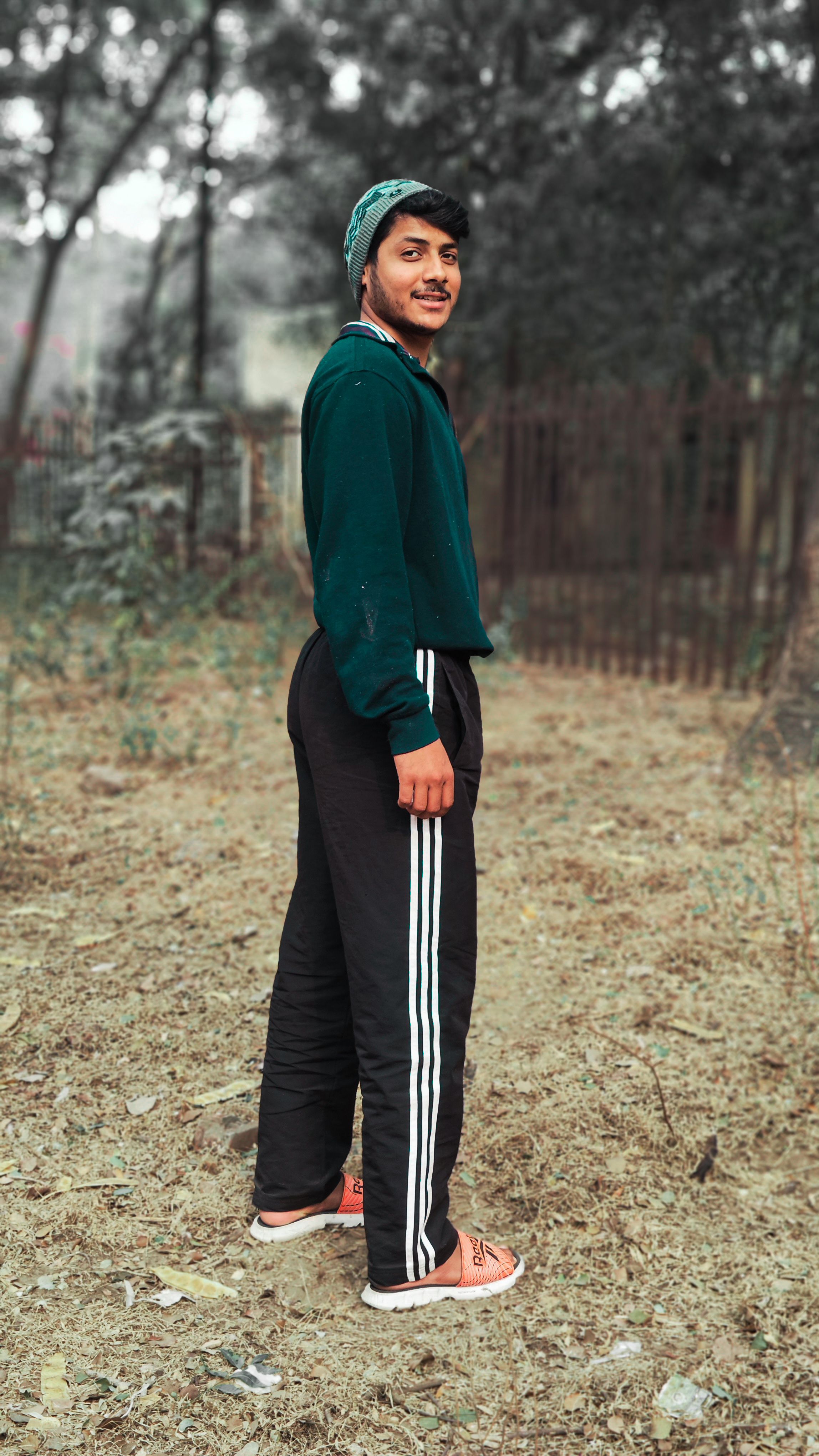 A young man smiling while standing outdoors in casual sportswear, enjoying a rural setting.