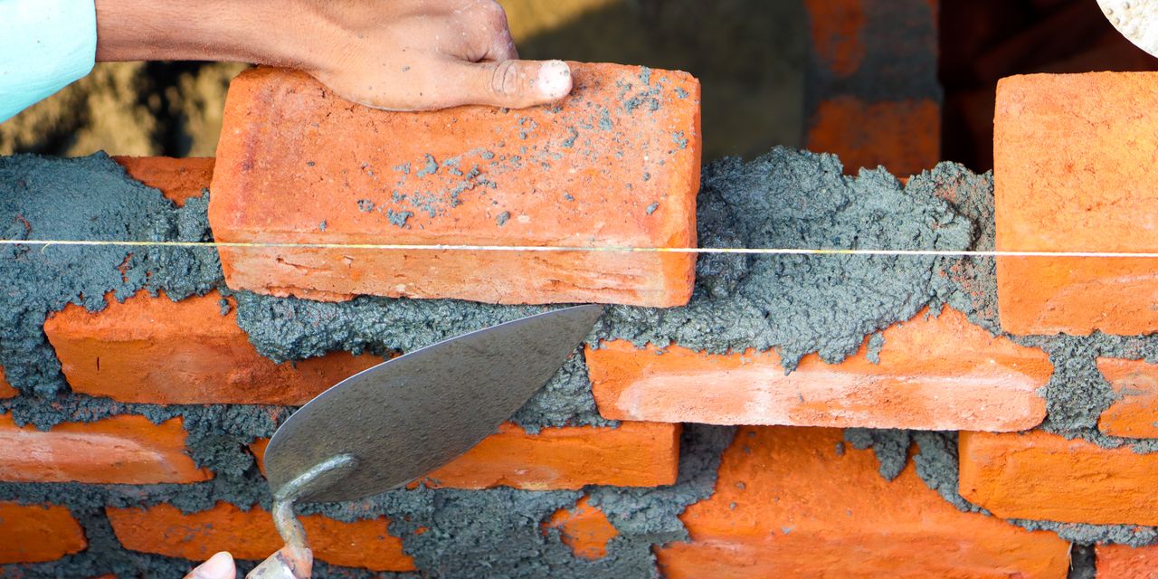 Hands laying bricks with cement in a construction setting, showcasing precise masonry work.