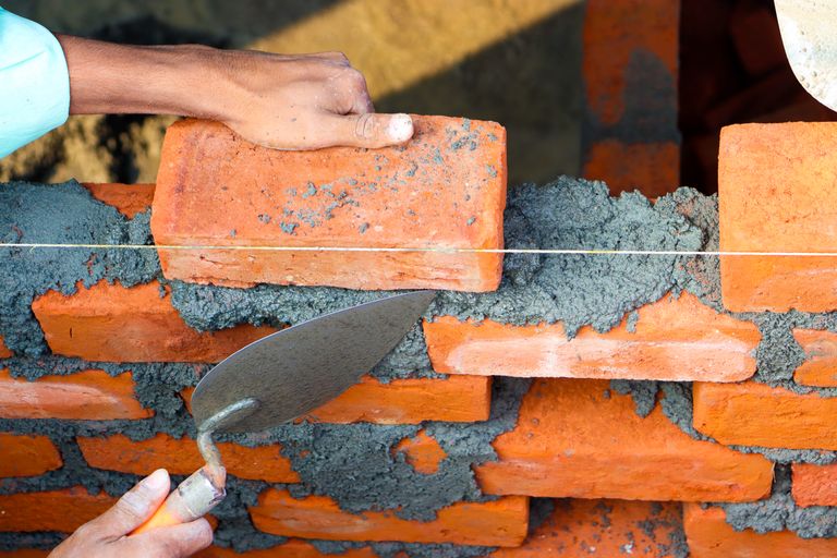 Close-up of a mason laying bricks with cement during a quality check