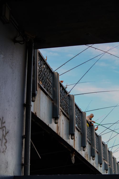 Free View of a person fishing on a steel urban bridge, set against a clear blue sky. Stock Photo