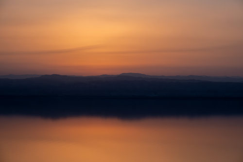 Free Beautiful sunset view over a calm lake with silhouetted mountains, capturing tranquility and natural beauty. Stock Photo