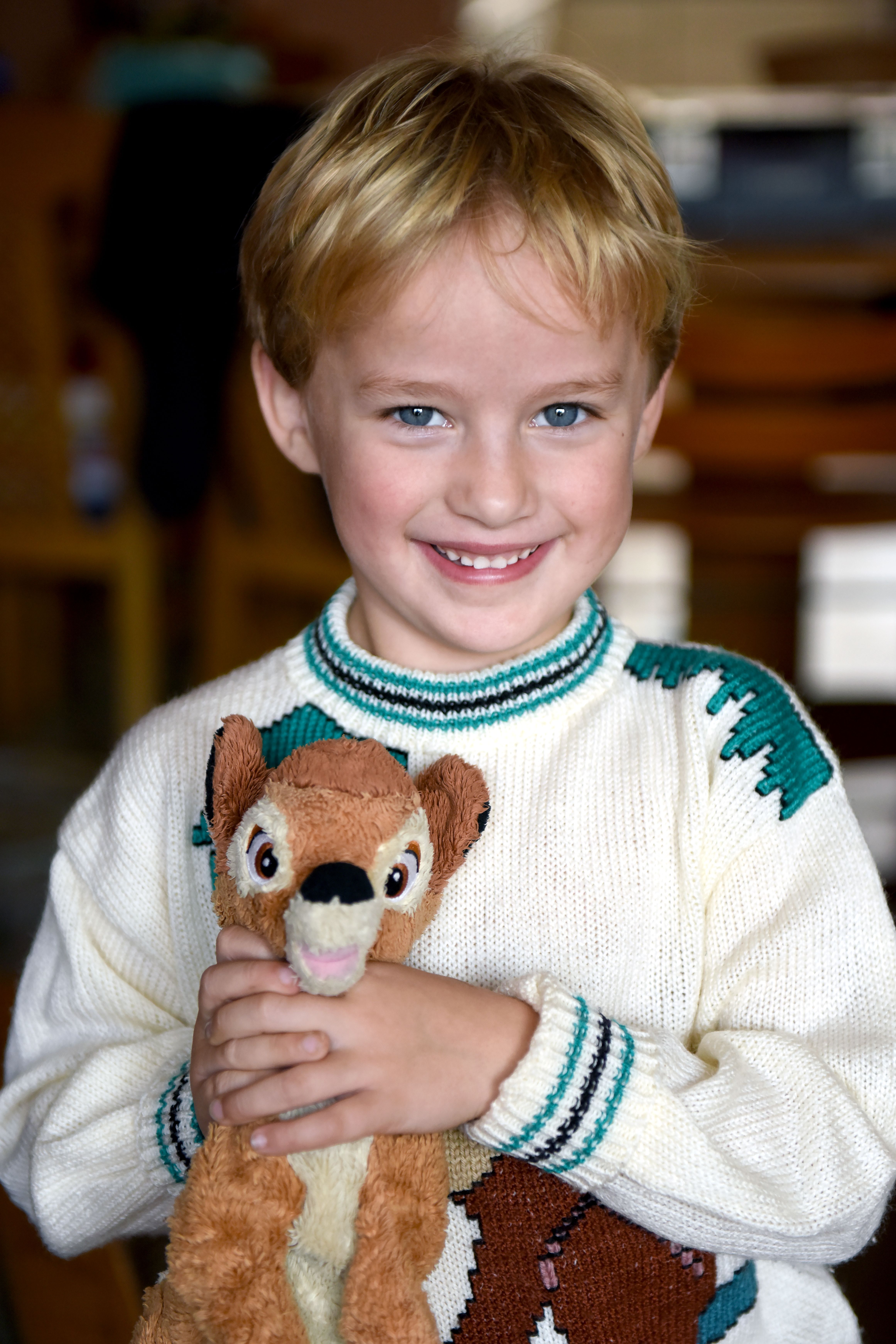 A cheerful young boy holding a plush deer toy, smiling warmly in a cozy room.