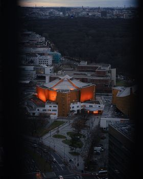 A dramatic aerial view of Berlin's Philharmonie illuminated against the evening cityscape.