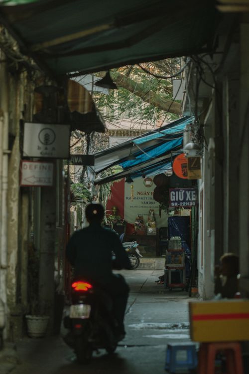 Free Rear view of a person on a scooter riding through a narrow urban alleyway. Stock Photo