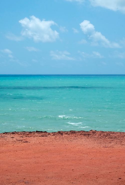 Free A beautiful view of a beach with red sandy shore and azure ocean under a clear blue sky Stock Photo