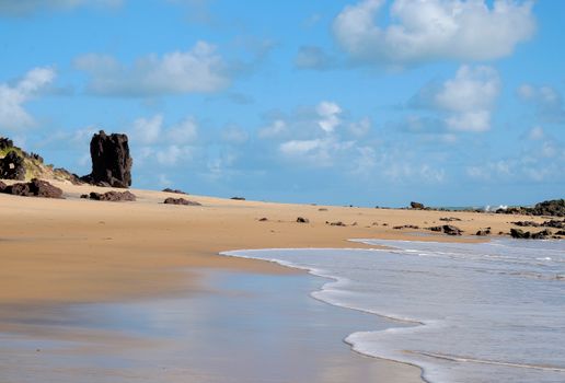 Serene coastal view with soft sands, rocks, and a stunning blue sky.