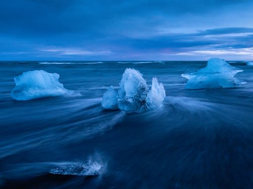 Free Captivating icy formations glisten along the shores of Diamond Beach under a serene twilight sky. Stock Photo