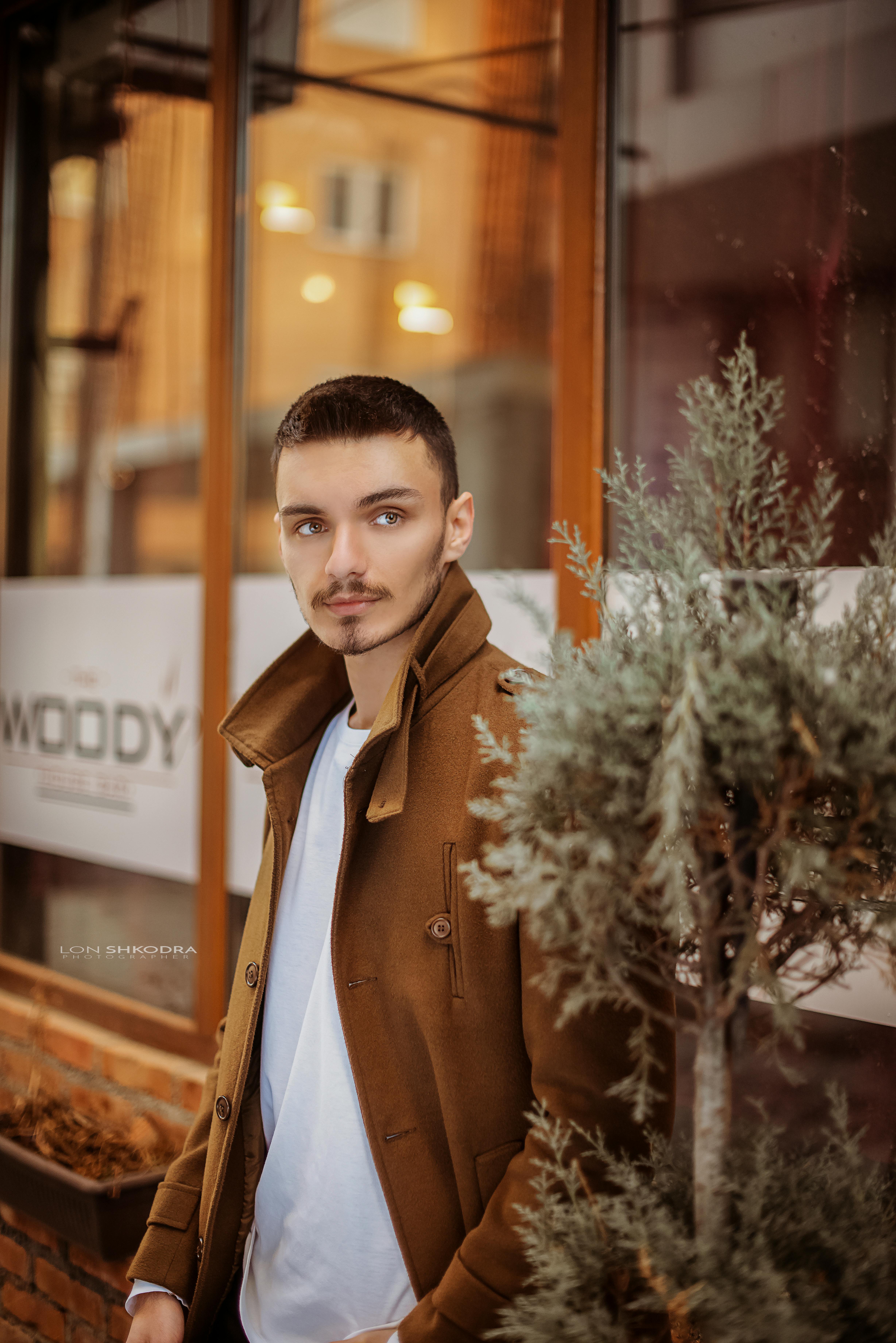 一位时尚男子穿着棕色外套，优雅地站在一家舒适的咖啡馆外