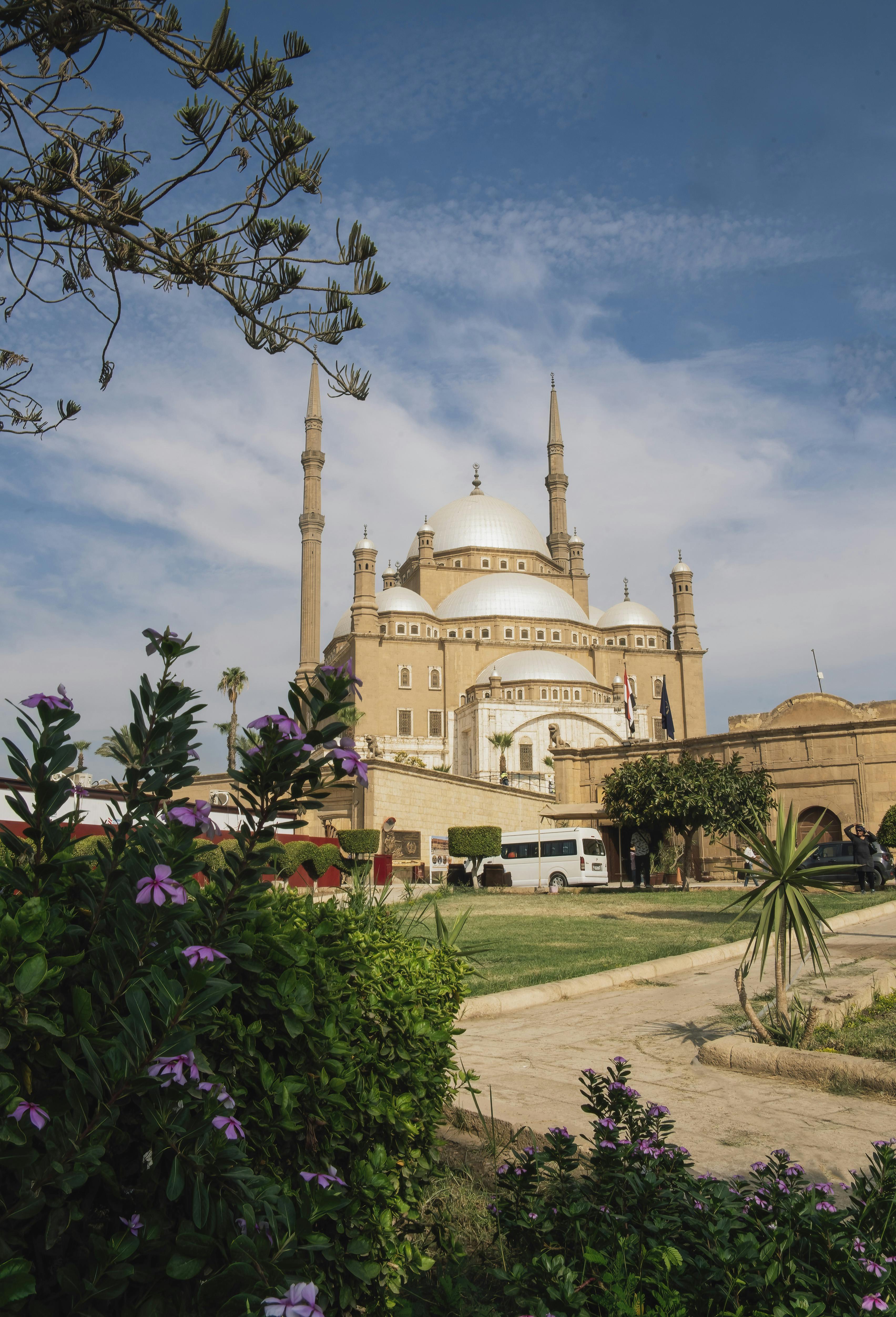 A picturesque outdoor view of the Muhammad Ali Mosque in Cairo, surrounded by lush gardens and blue skies.