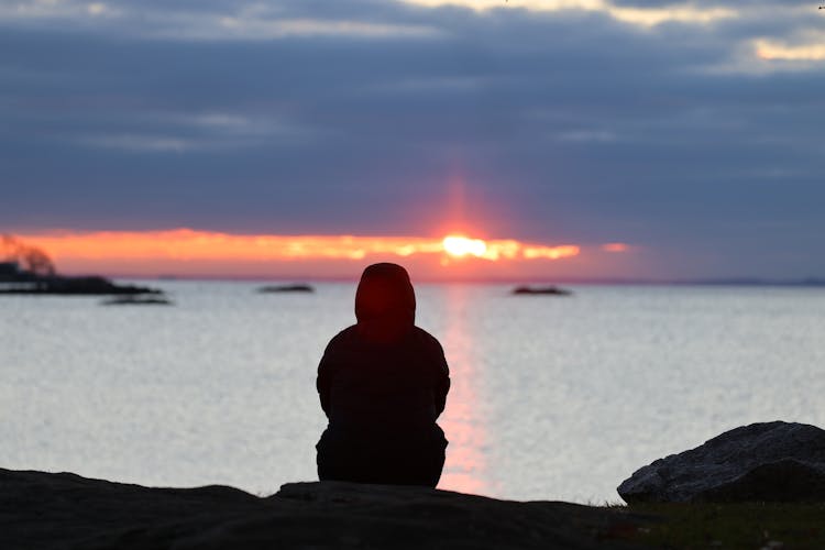 Silhouette Of Person Sitting On Rocks On Sunset