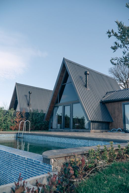 Steep-roofed house beside a planted poolside terrace — photo by Gokhan Yetimova on Pexels
