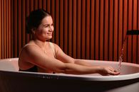 A woman enjoys a relaxing bath, smiling as water flows, in a stylish modern bathroom.