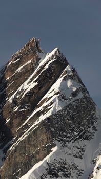 Snow-draped mountain peak with rocky textures against a clear sky at sunrise.