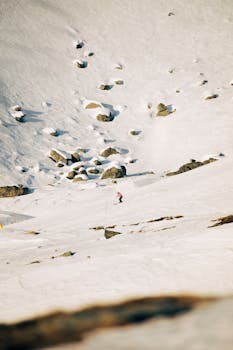 Solo skier gliding down a snowy mountain slope amidst rugged alpine terrain.