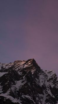 A breathtaking view of a snowy mountain peak under a purple-hued twilight sky.