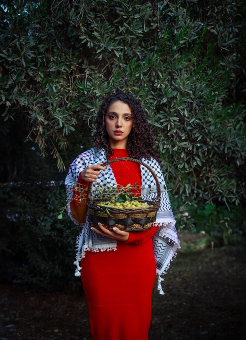 Free A woman in a red dress holding a basket of grapes, standing outdoors in front of lush greenery. Stock Photo