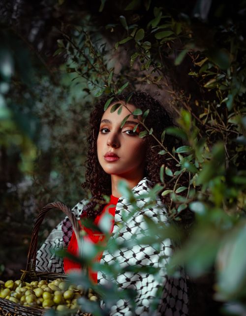 Free Middle Eastern woman in traditional attire holding a basket of fruit, surrounded by foliage. Stock Photo
