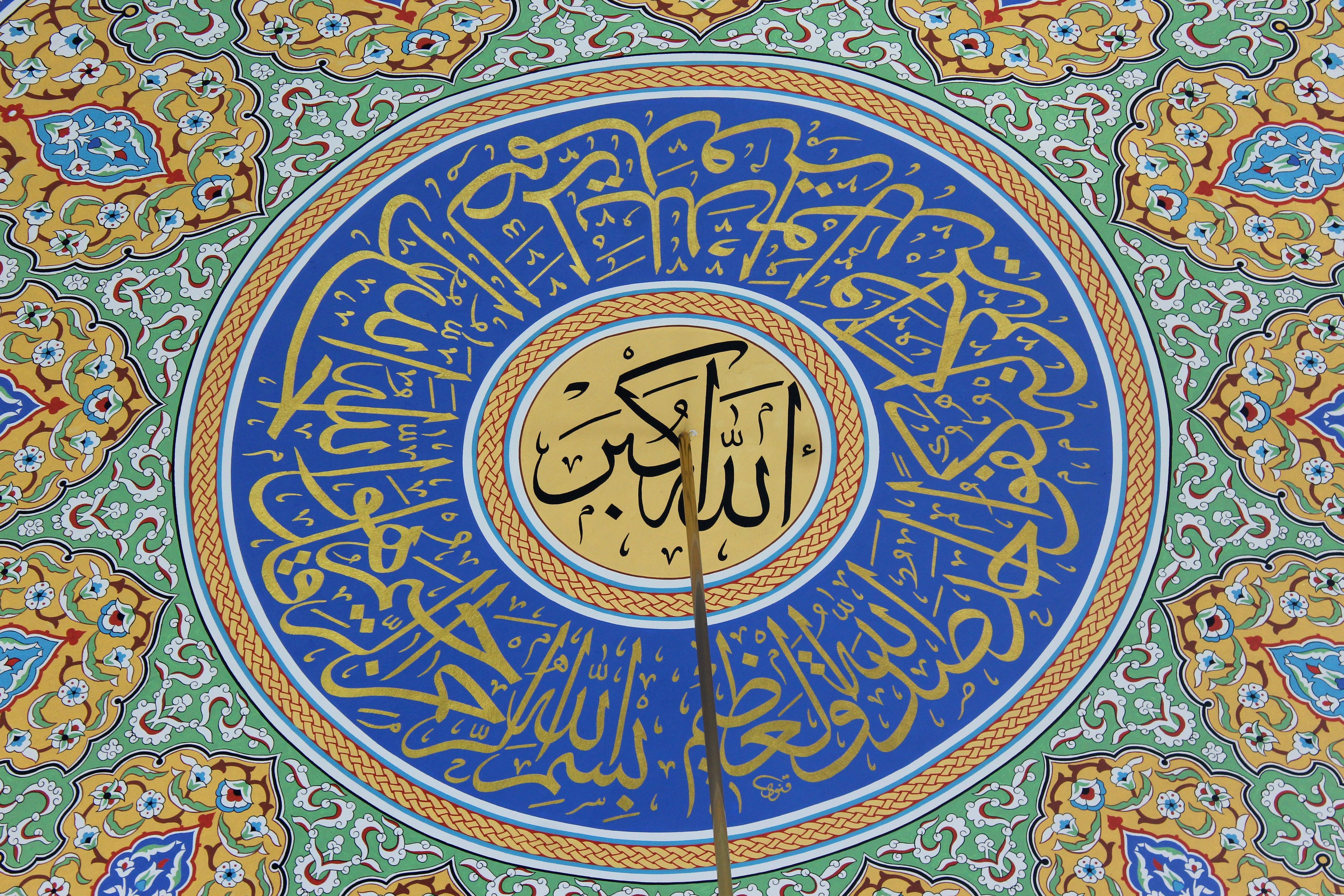 A beautifully ornate Islamic ceiling featuring intricate Arabic calligraphy and colorful geometric patterns.