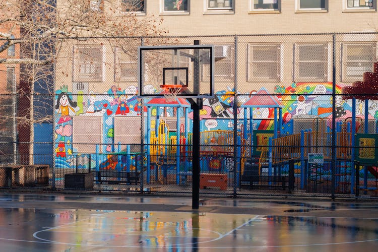 A Basketball Court Next To A Playground And Building With Colorful Illustrations