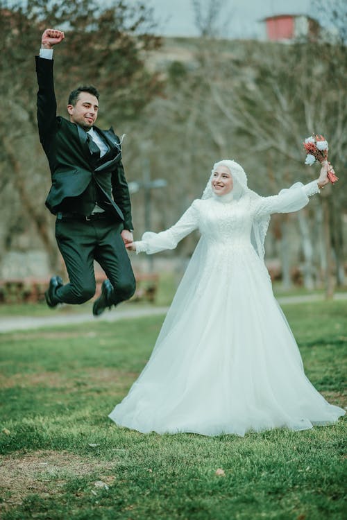 Bride and Groom Holding Hands and Jumping in a Park 