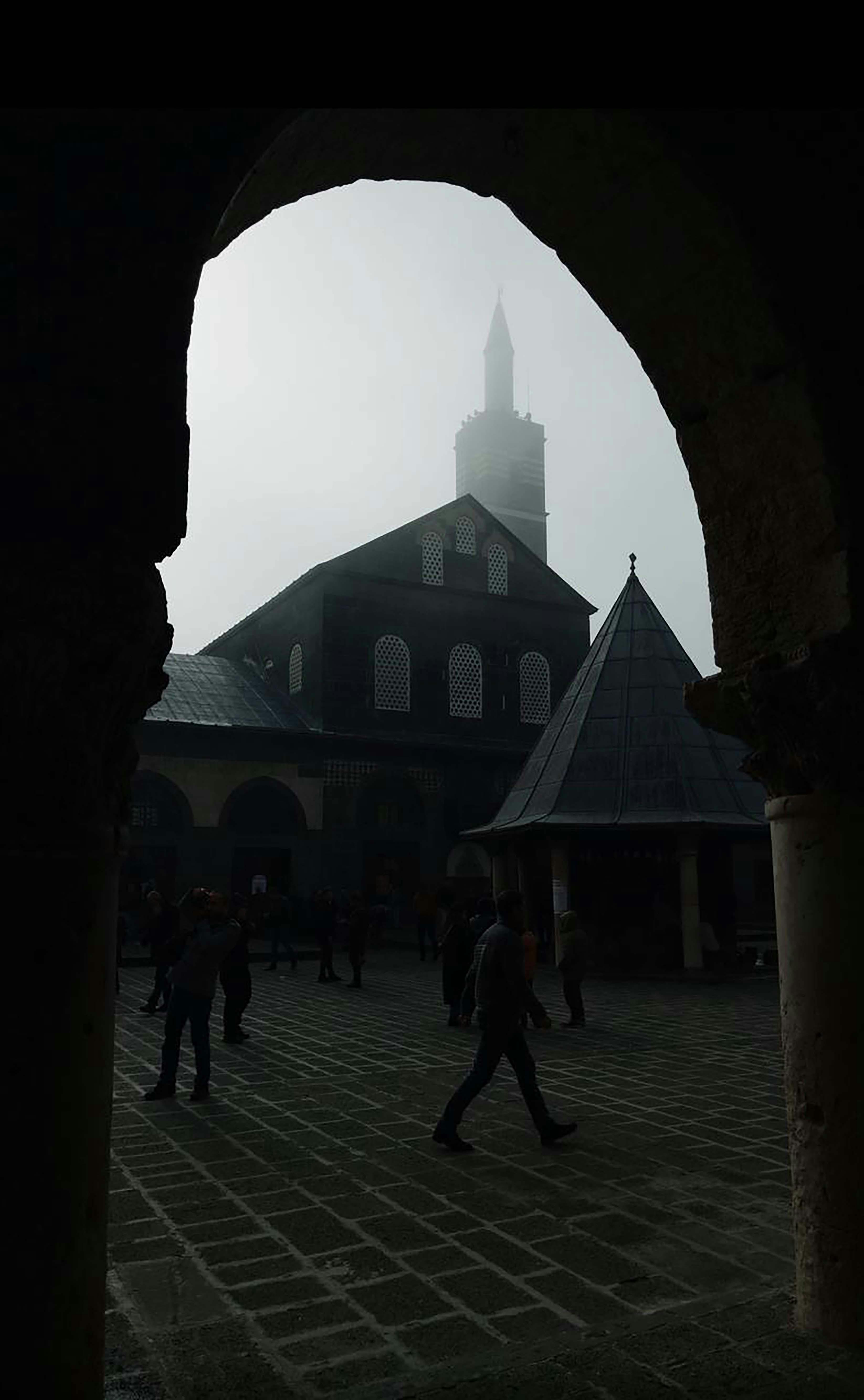 passersby in the courtyard of the great mosque of diyarbakir on a foggy day