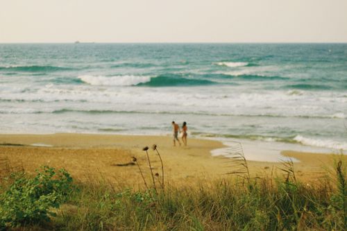 Free A couple enjoys a romantic walk on a serene sandy beach with gentle ocean waves. Stock Photo