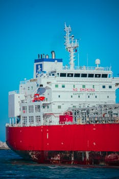 A large red cargo ship sailing in the open sea under a clear blue sky, showcasing marine logistics.