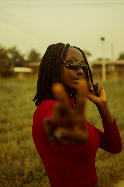 Free A fashionable woman with braided hair and sunglasses poses outdoors, making a peace sign on a sunny day. Stock Photo