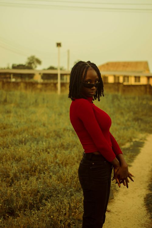 Free Fashionable woman in red top and sunglasses standing in rural Nigerian setting. Stock Photo