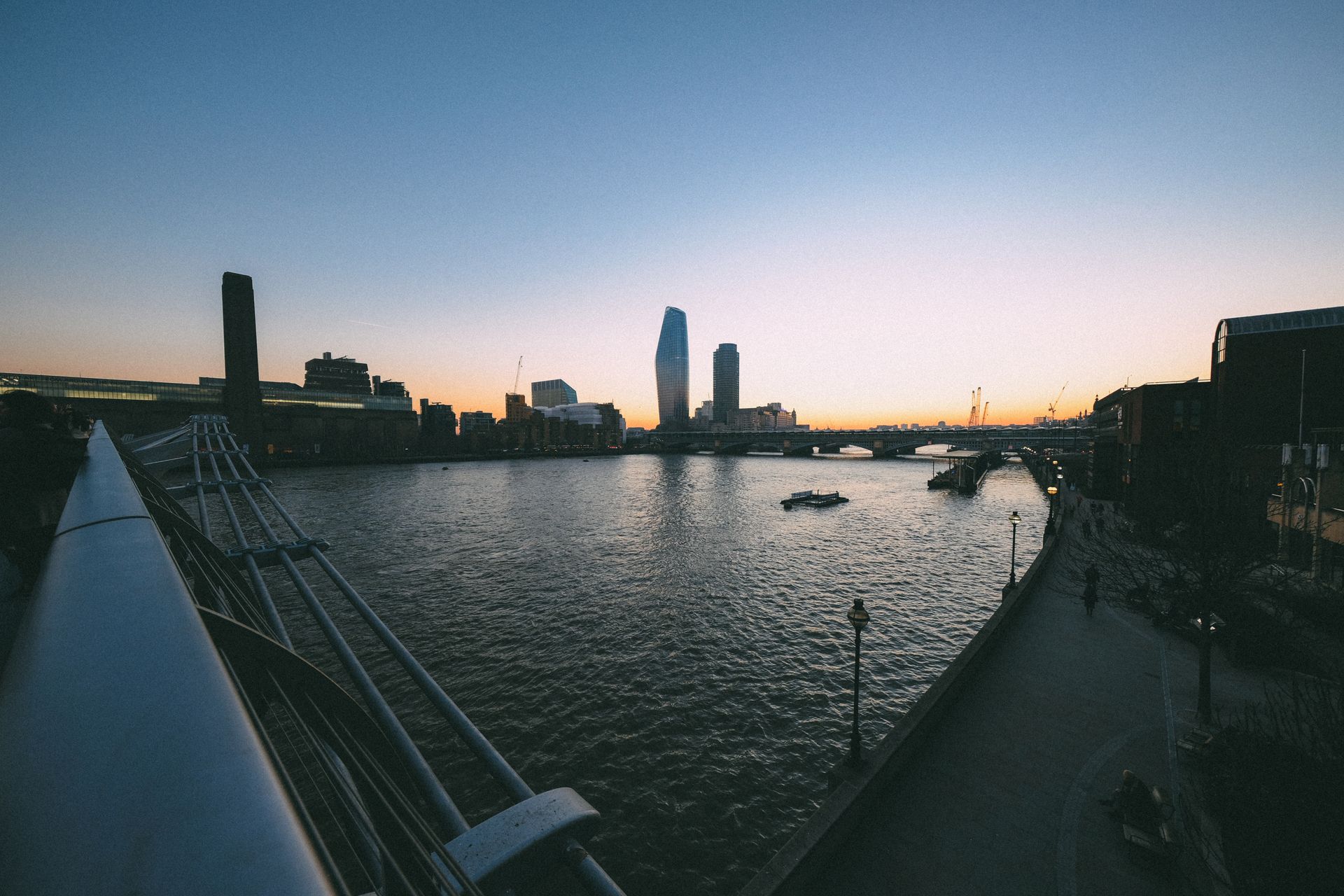 A breathtaking view of a city skyline and river during sunset with a prominent modern bridge.