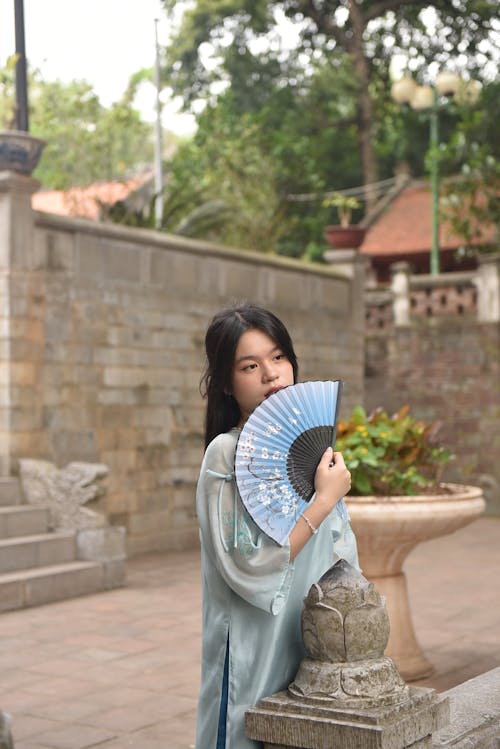 Young Woman in a Blue Ao Dai Tunic Holding a Paper Fan