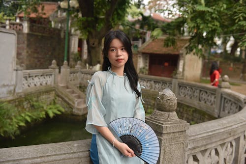 Young Model with a Blue Floral Fan Wearing Ao Dai Dress by the Pond