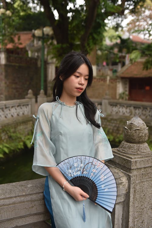 Young Model in a Blue Ao Dai Tunic Holding a Paper Fan in the Temple Gardens