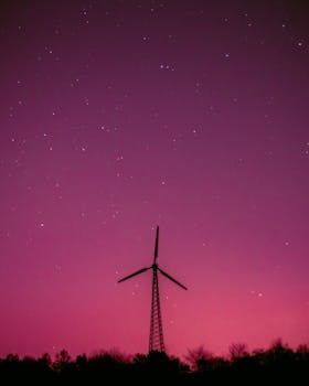 在充满活力的紫色天空和星星映衬下，风力涡轮机的轮廓象征着可再生能源