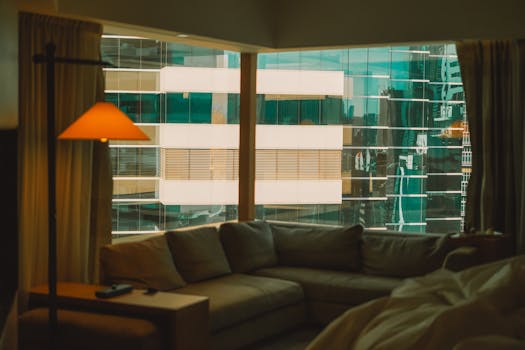 Modern living room with a cityscape view through large windows and soft ambient lighting.