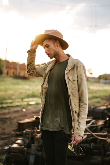 Portrait of a fashionable man in a hat posing outdoors at sunset, exuding casual style.