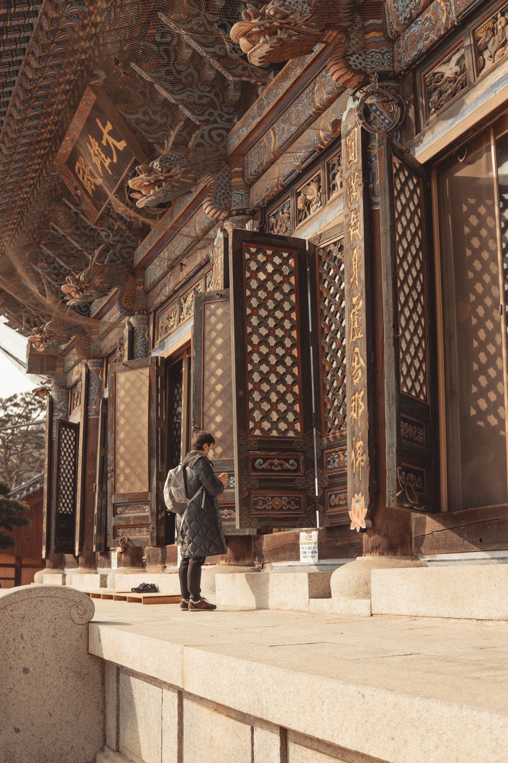Woman praying outside Buddhist temple with traditional architectural details in South Korea