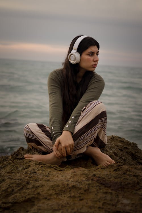 Young Woman with Headphones Sitting on Seashore