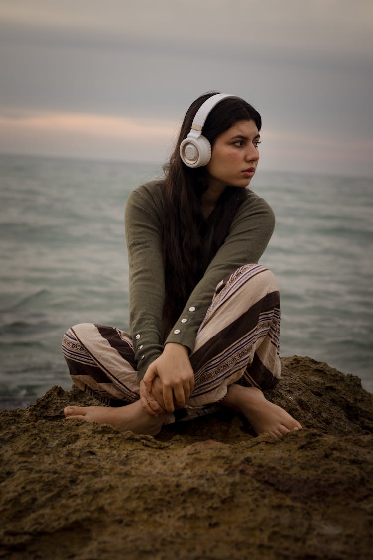 Young Woman With Headphones Sitting On Seashore