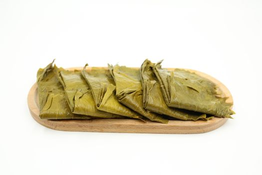 Freshly prepared tamales wrapped in banana leaves on a wooden plate against a white background. Perfect for authentic food photography.