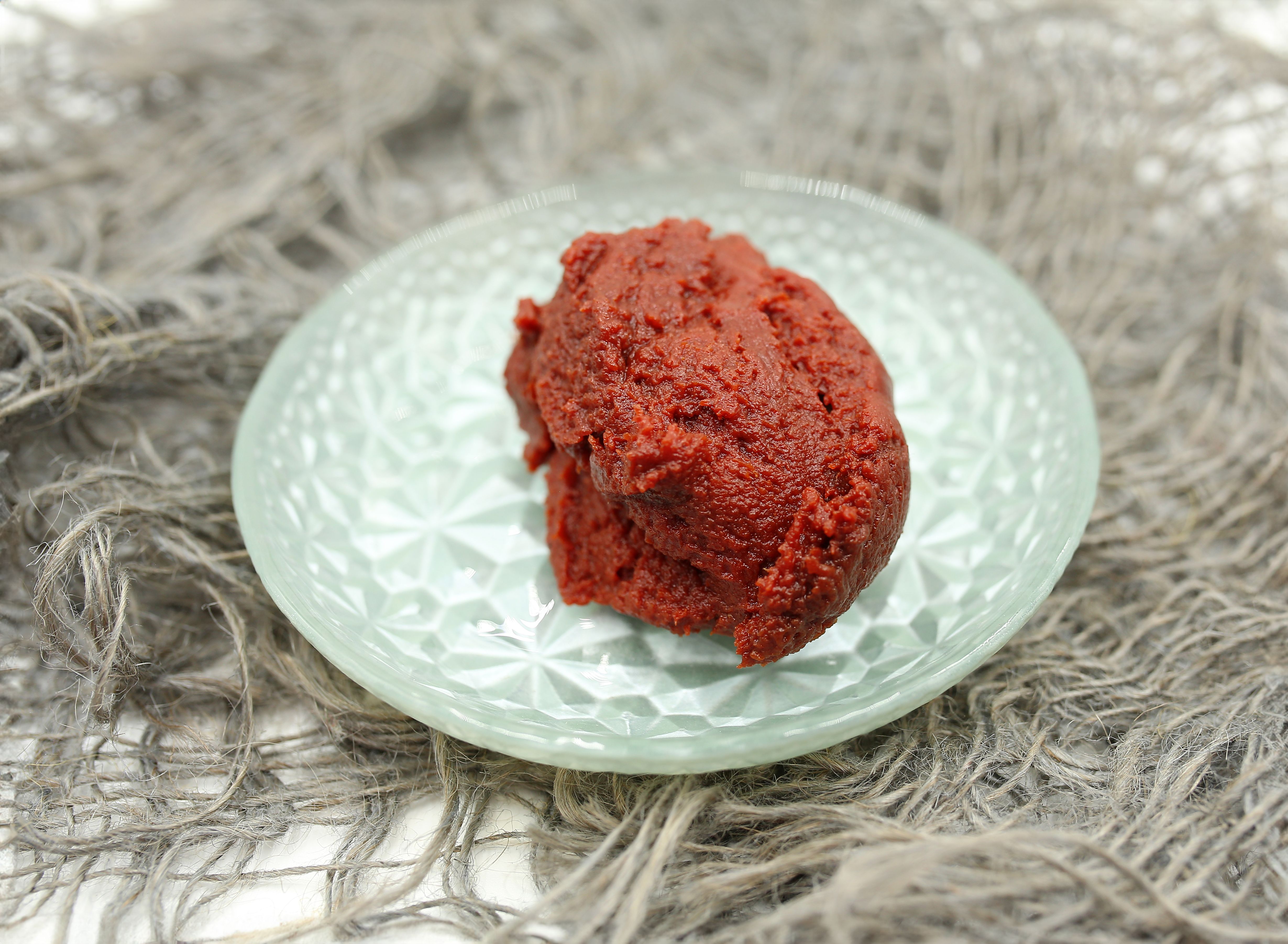 A scoop of red paste served on a decorative glass plate, perfect for various culinary applications.