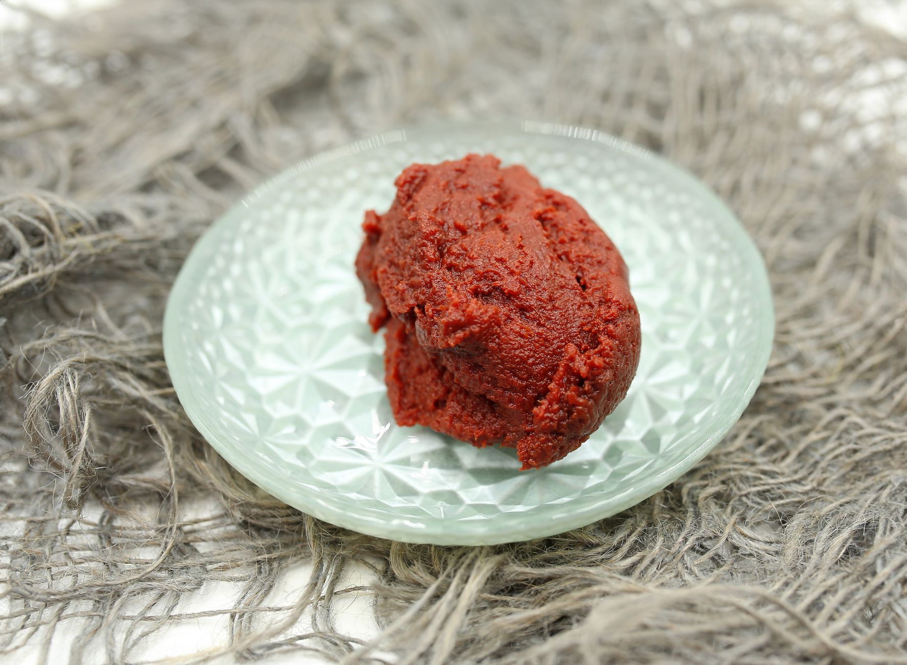 A scoop of red paste served on a decorative glass plate, perfect for various culinary applications.