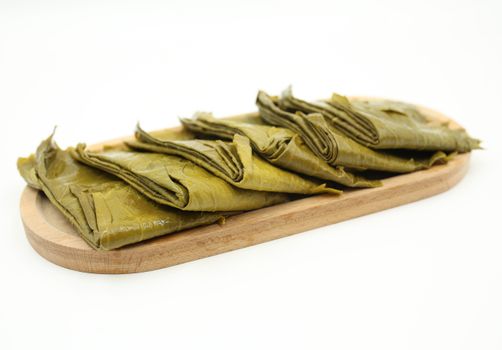 Delicious stuffed grape leaves neatly arranged on a wooden plate against a white background.