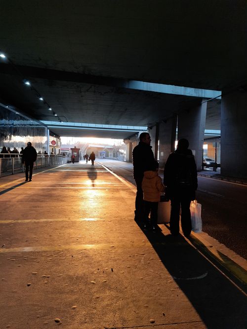Free Silhouettes of people wait at sunset under a city bridge, capturing urban life and light play. Stock Photo