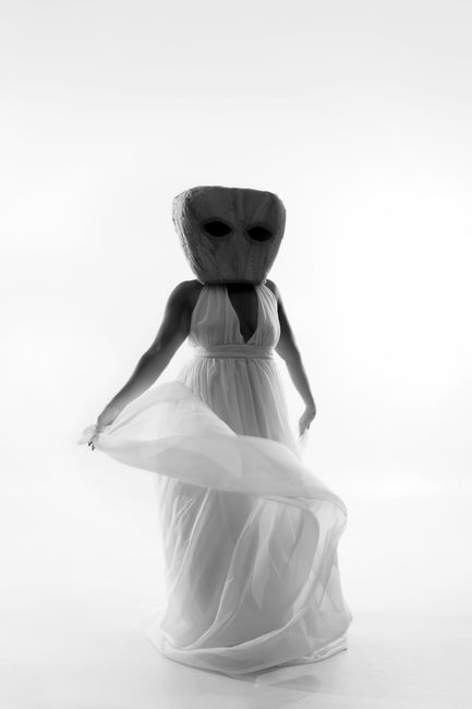 Elegant black and white photo of woman in flowing dress and artistic mask, showcasing unique fashion.