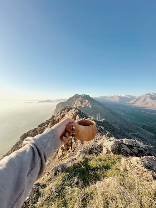 Person Standing on Top of a Mountain and Holding a Cup 