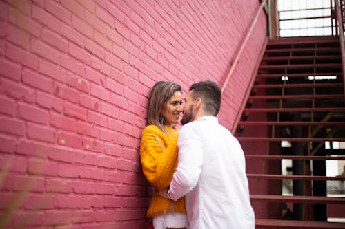 남자와 여자 키스하려고 붉은 벽돌 벽 옆에 서있는